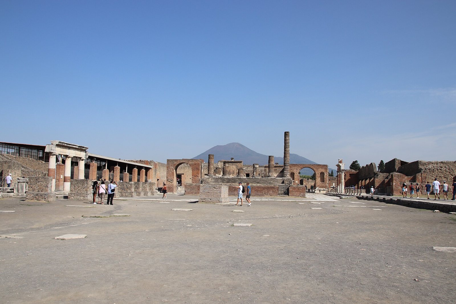 Il Foro di Pompei con i resti del Tempio di Giove e le colonne antiche, sullo sfondo il profilo del Vesuvio sotto un cielo azzurro