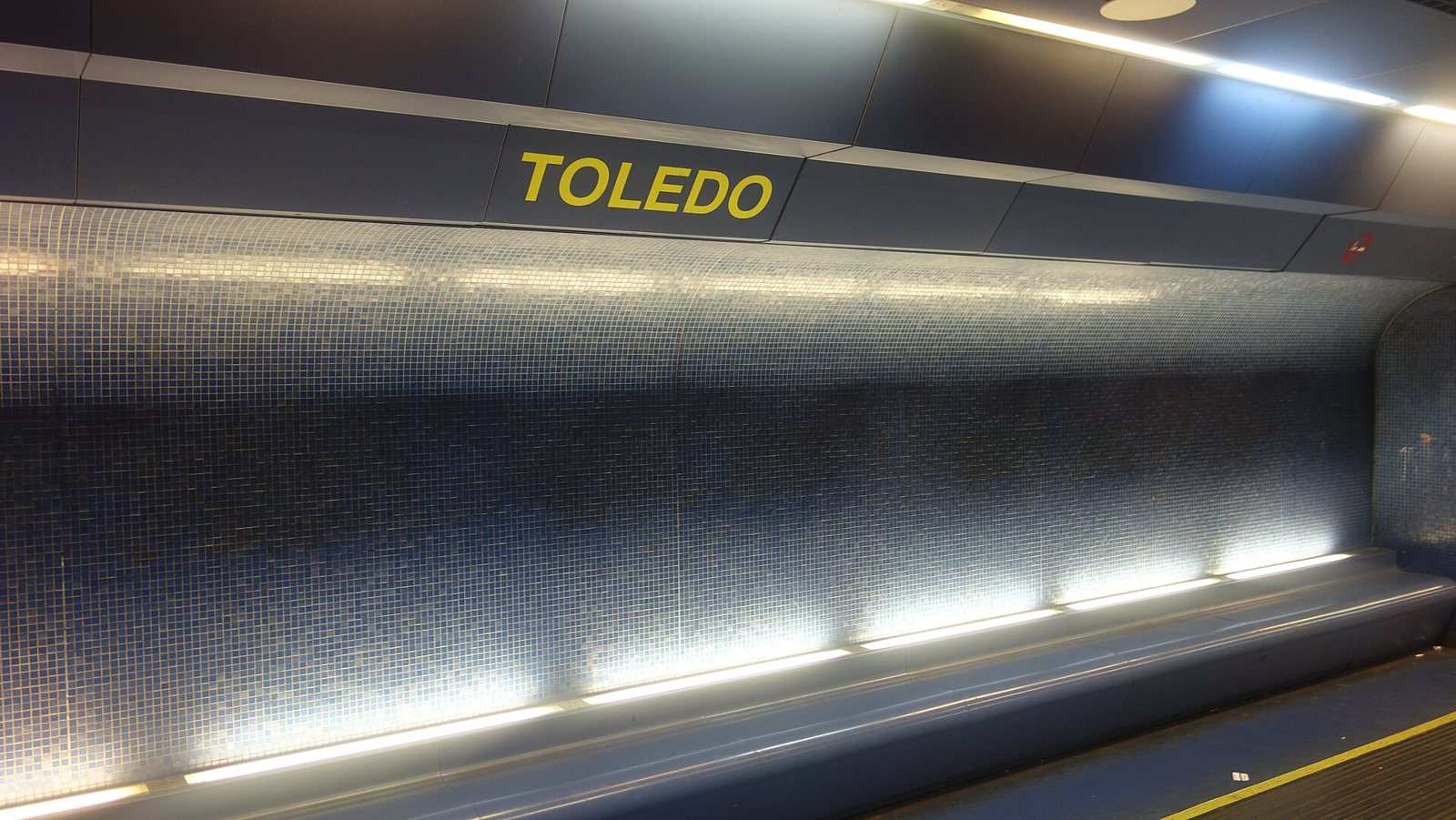 Banchina della stazione Toledo della metropolitana di Napoli, con la scritta TOLEDO gialla e la parete a mosaico blu illuminata