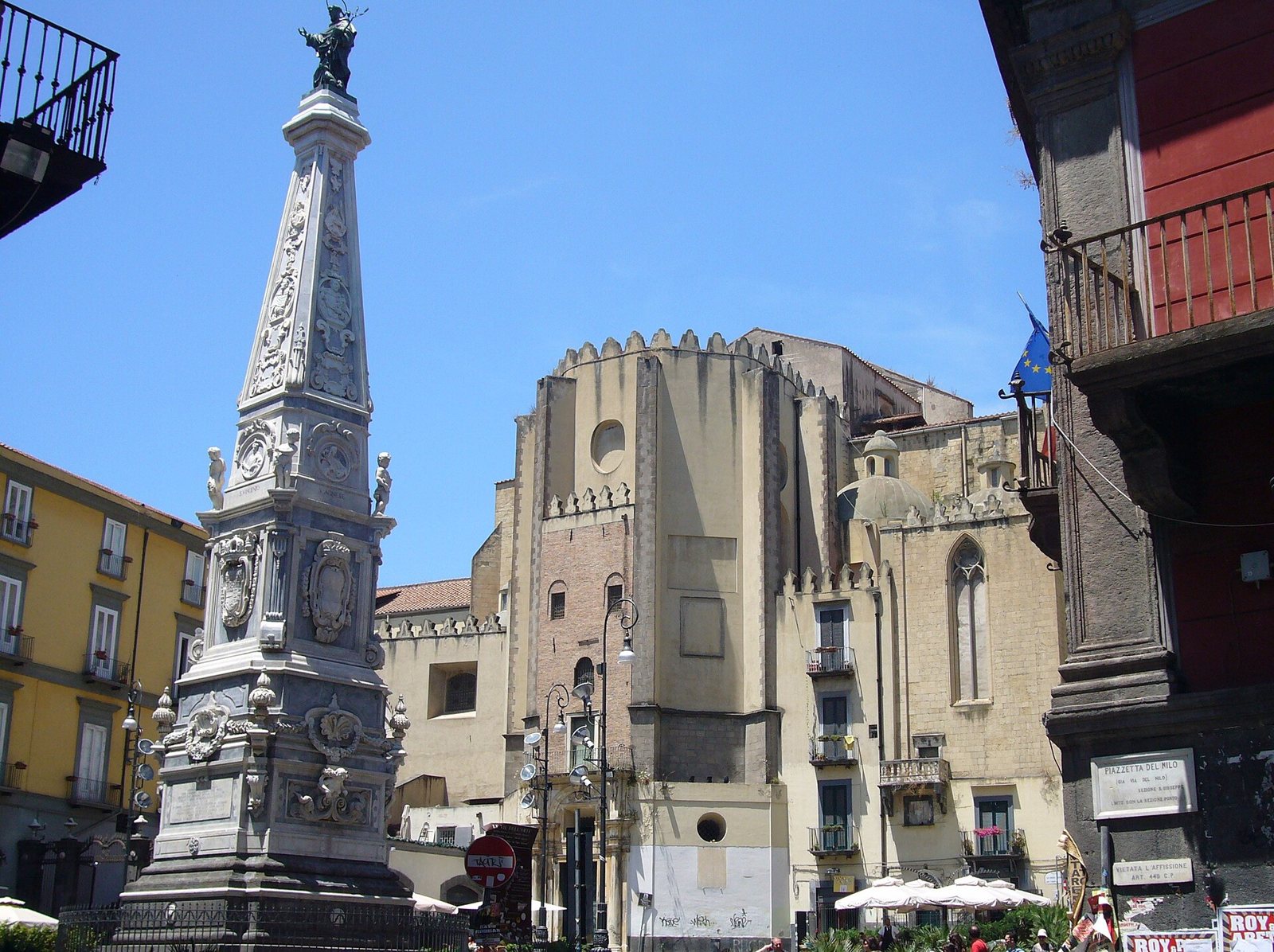 Piazza San Domenico Maggiore a Napoli con la guglia barocca in primo piano e l'abside della chiesa di San Domenico sullo sfondo