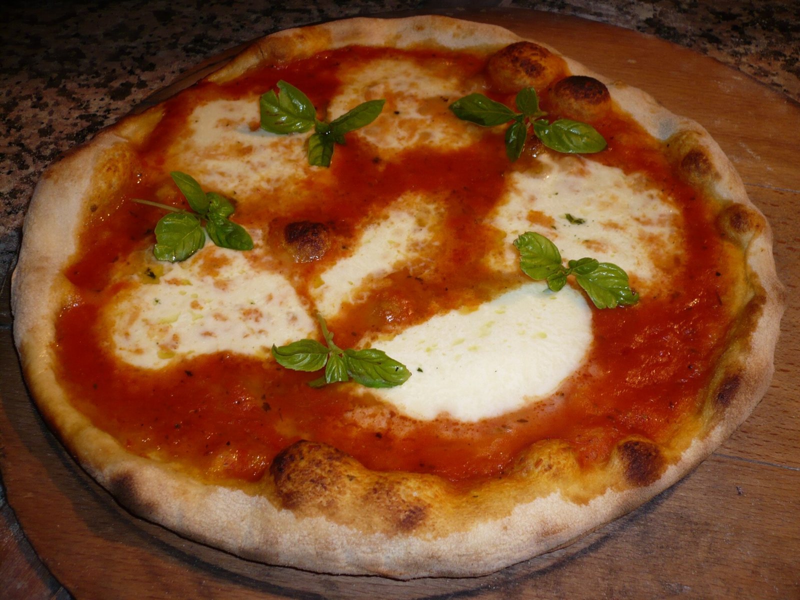 Pizza margherita napoletana con pomodoro, mozzarella fusa, foglie di basilico e cornicione bruciacchiato su un tagliere di legno