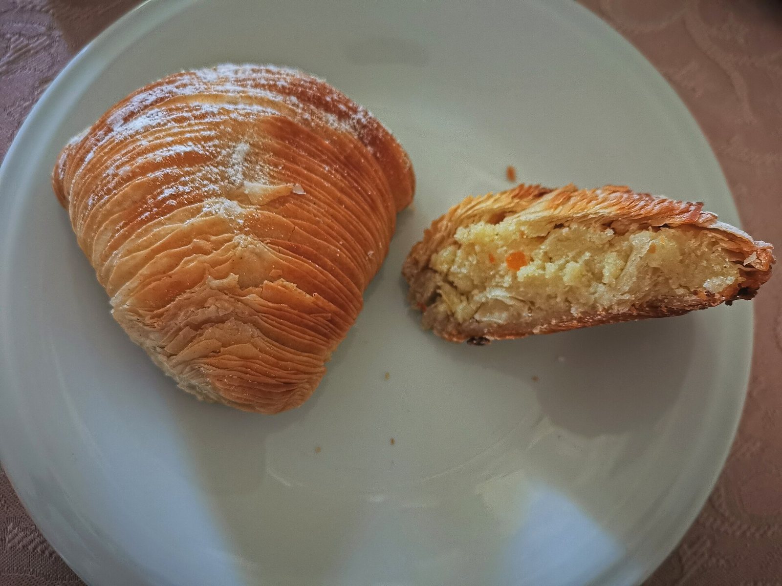 Sfogliatella riccia napoletana su un piatto bianco, intera e tagliata a metà con il ripieno di ricotta, semola e canditi in vista