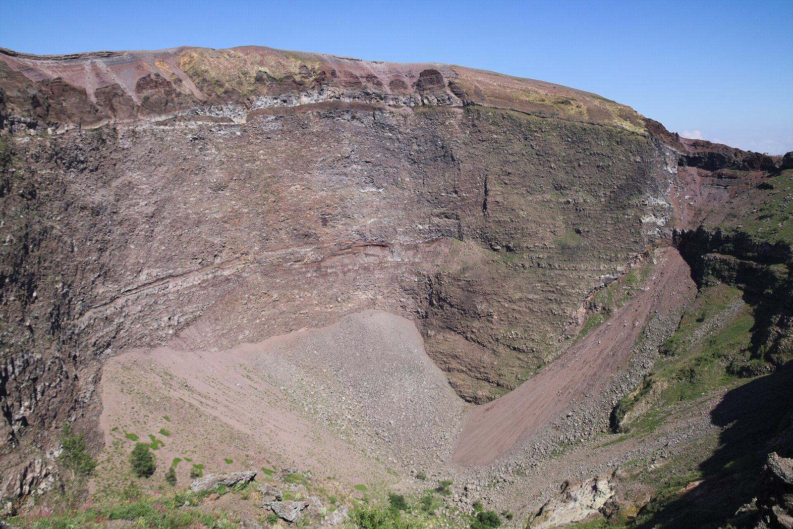 Interno del cratere del Vesuvio con le pareti rocciose stratificate e il fondo di detriti sotto un cielo azzurro
