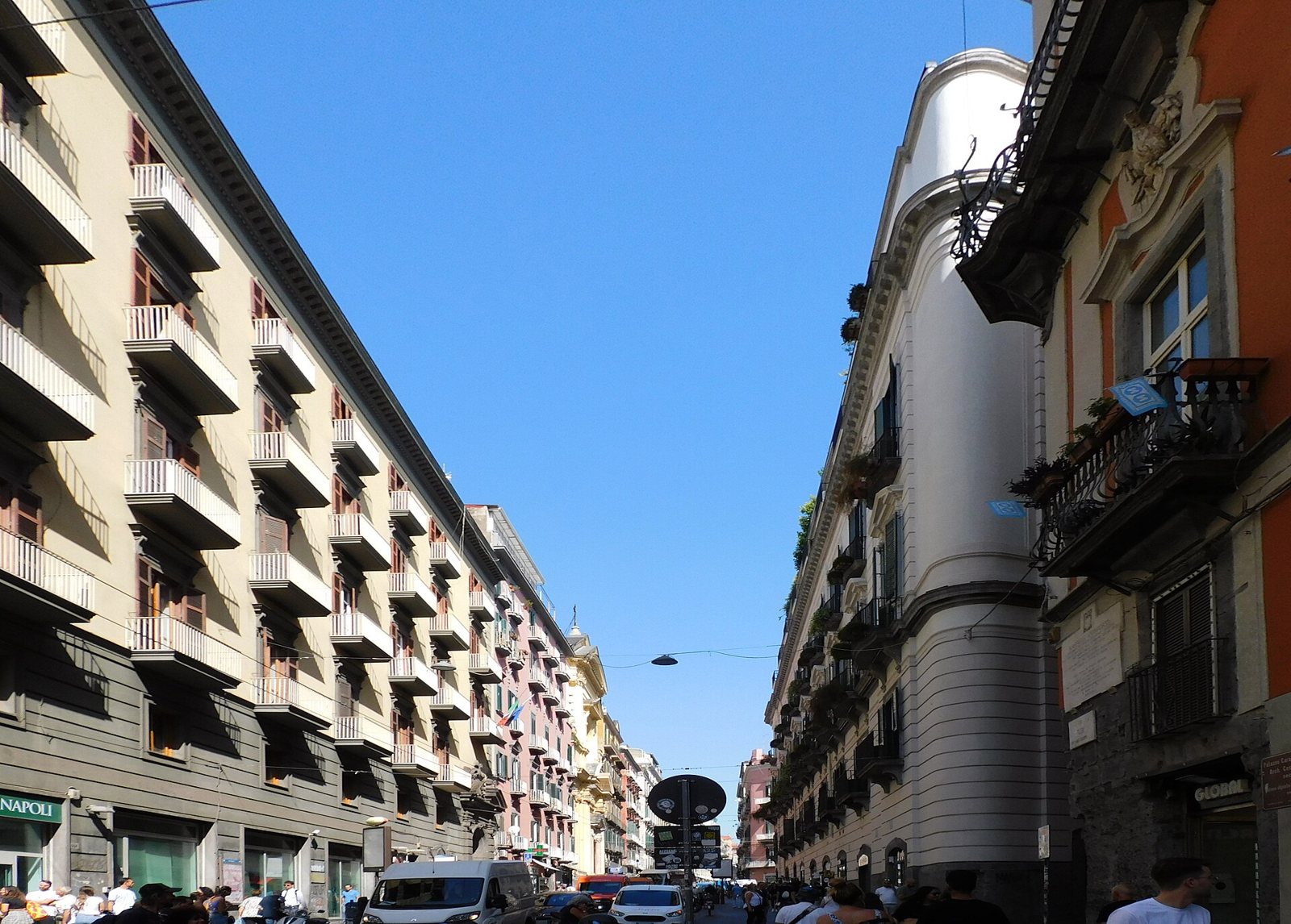 Via Toledo a Napoli in una giornata di sole, con palazzi storici dai balconi in ferro battuto e passanti lungo la strada